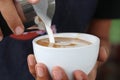 Barista pouring milk foam for making coffee latte art with pattern the leaves in a cup Royalty Free Stock Photo