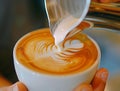 barista pouring milk latte art from silver pitcher into the hot coffee cup. Royalty Free Stock Photo