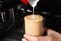 Barista pouring steamed milk from pitcher into glass cup of fresh aromatic coffee in cafe, closeup Royalty Free Stock Photo