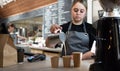 A barista prepares a fresh latte with milk in a cafe. Girl salesman in uniform pours milk into paper cups with coffee in Royalty Free Stock Photo