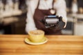 Barista standing near bar counter pay bill using cell application and pos machine Royalty Free Stock Photo