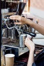 Barista steaming milk for hot cappuccino in tin pitcher