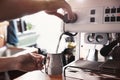 Barista steaming milk in metal jug with coffee machine wand at bar counter Royalty Free Stock Photo