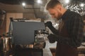 Barista steaming milk in pinscher. Portrait of bearded concentrated barista preparing cappuccino in a coffee shop. Cafe owner is Royalty Free Stock Photo