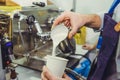 Barista using coffee machine preparing fresh coffee and pouring milk to espresso coffee make latte art into white paper cup at cof