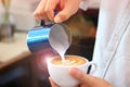 Barista using pitcher for pouring frothed milk to cup of coffee latte tulip pattern on top