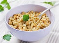 Barley porridge in a bowl with meat, vegetables and green parsley