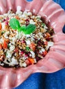 Barley salad with pomegranate, feta and mint on a pink ceramic and denin napkin