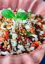 Barley salad with pomegranate, feta and mint on a pink ceramic and denin napkin