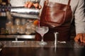 Barman in a brown apron pours from a steel shaker alcohol cocktail Royalty Free Stock Photo