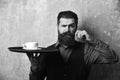 Barman with confident face brings tea or coffee. Waiter with white tea cup on tray. Man with beard