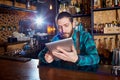 Barman with a hipster beard looks at laptop behind counter in