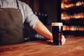 Barman hold dark cold fresh beer to client in pub behind bar. Blur background