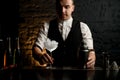 Barman holds transparent glass full of ice which stands on bar counter.