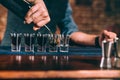 Bartender pouring strong alcoholic drink into small glasses on bar counter