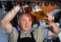 Barman is pouring unbottled beer with foam for client in the bar.