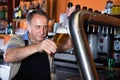 Barman is pouring unbottled beer with foam for client in the bar.