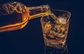 Barman pouring whiskey with ice cubes in glass on black background, cool atmosphere