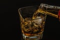 Barman pouring whiskey with ice cubes in glass on black background, cool atmosphere Royalty Free Stock Photo