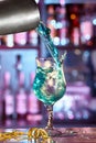 The barman pours a blue lagoon cocktail from a shaker into a beautiful glass on a thin leg.