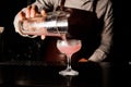 Barman preparing and pouring cosmopolitan alcoholic pink cocktail at bar.