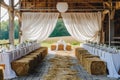 A barn filled with neatly stacked hay bales and tables covered in crisp white linens, A rustic barn setting with hay bales and