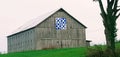 A barn with an ornamental barn quilt in a green horse field