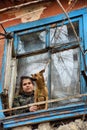 A girl with a dog in a poor quarter looking out the window of an old house Royalty Free Stock Photo