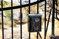 A barred gate with an old mailbox, against the background of a small white house and an overgrown garden.