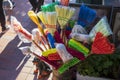 A barrel of colorful brooms and mops for sale with a small dog statue and people walking at Olvera Street in Los Angeles