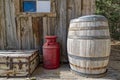 A barrel, a metal jug, and a trunk on the porch of an old wood cabin