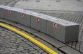 Stone blocks connected by metal strips. The unit acts as a road barrier with traffic arrows in a bend. A heavy chain protects the