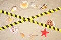 Barrier tape - quarantine, isolation, entry ban. Seashells and nautical rope decoration on sand background with red toy ship