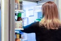 Woman choosing food from open refrigerator