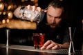 Bartender with beard pouring alcohol cocktail using glass with strainer