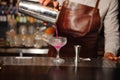 Bartender pours from a steel shaker into a cocktail glass a lilac-colored alcohol cocktail Royalty Free Stock Photo