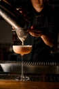 bartender gently pours drink into glass by filtering it through sieve.