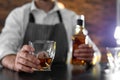 Bartender with glass and bottle of whiskey at counter in bar, closeup. Royalty Free Stock Photo