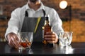 Bartender with glass and bottle of whiskey at counter in bar, closeup. Royalty Free Stock Photo