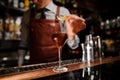 Bartender with glass and lemon peel preparing cocktail at bar