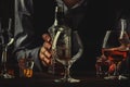 The bartender holding bottle of strong drink in hand and big wine glass on the old bar counter. Vintage wooden background in pub Royalty Free Stock Photo