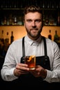 bartender holds transparent glass of alcoholic cocktail garnished with orange peel Royalty Free Stock Photo