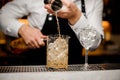 Bartender pouring alcoholic drink into a large glass filled with ice cubes Royalty Free Stock Photo