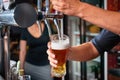 Bartender pouring beer from tap behind bar. Blurred woman in the background