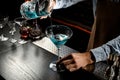 Bartender pouring a blue color alcoholic cocktail from the measuring cup with strainer to a martini glass Royalty Free Stock Photo