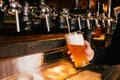 Bartender pouring light, cold foamy beer from tap into glass at bar with multiple beer dispensers. Serving craft beer Royalty Free Stock Photo