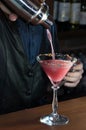 Bartender pouring pink alcohol drink into glass on high stem glass from silver metal sheker