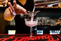 Bartender pouring a pink cocktail into a glass through a strainer - concept of alcohol