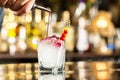 Bartender is pouring syrup to a glass with cocktail at bar