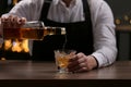 Bartender pouring whiskey from bottle into glass at bar counter indoors, closeup Royalty Free Stock Photo